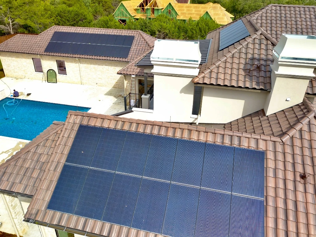 Aerial view of a suburban house roof with two large solar panel arrays installed on either side of a central chimney.