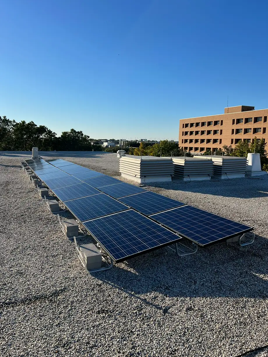 Row of solar panels installed on a flat gravel rooftop under a clear blue sky.