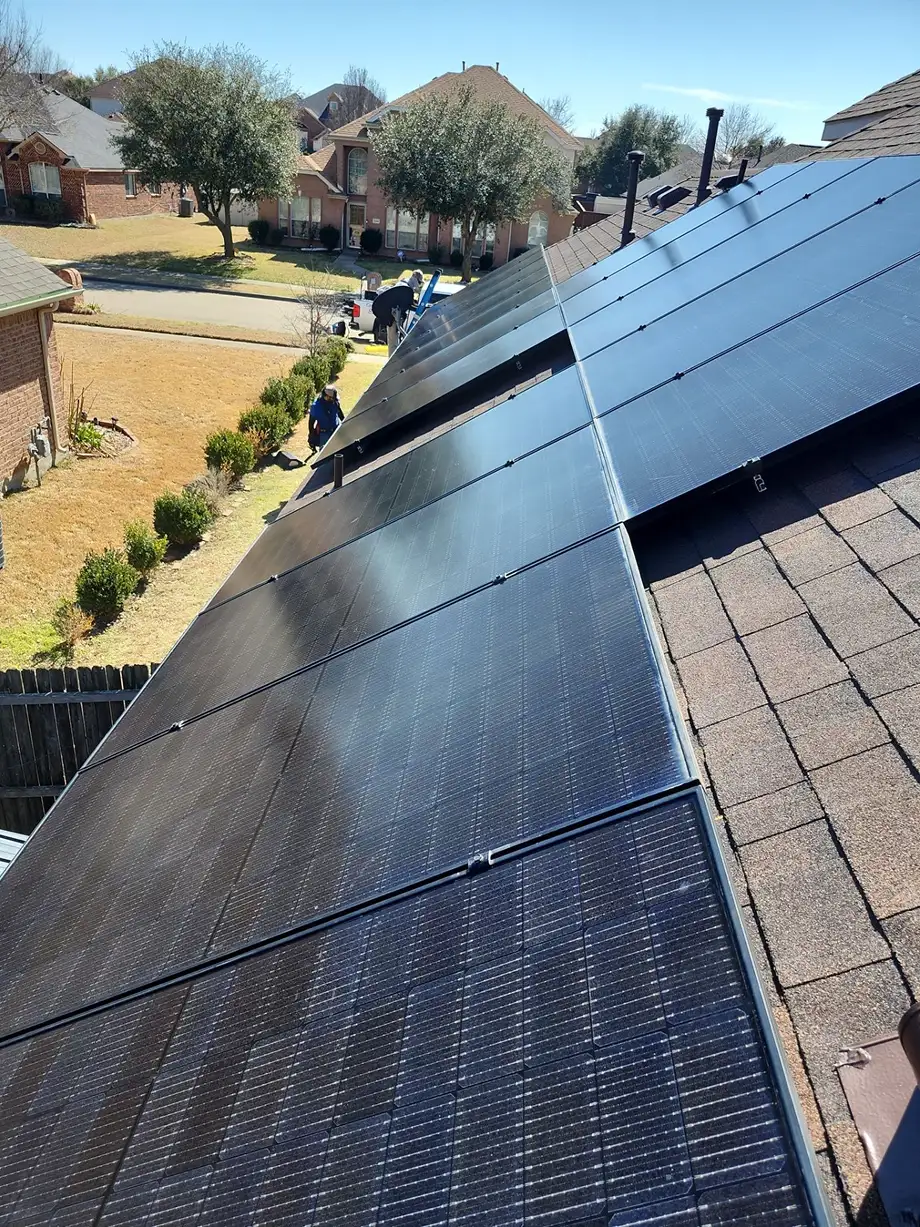 Solar panels installed on a slanted residential roof with houses and trees in the background.